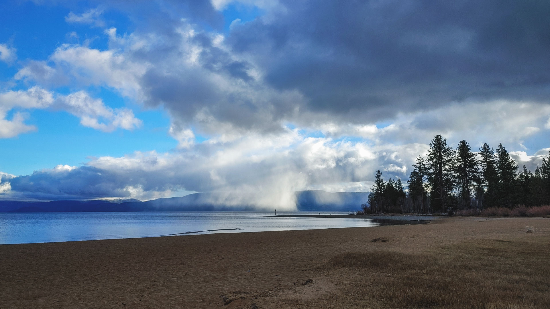 Clouds and mist over lake with pine trees and a beach